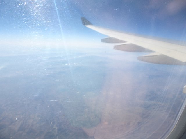 Haze in a sunny blue sky and reflection on a plane window during flight with a view of the wing in a transport and travel concept