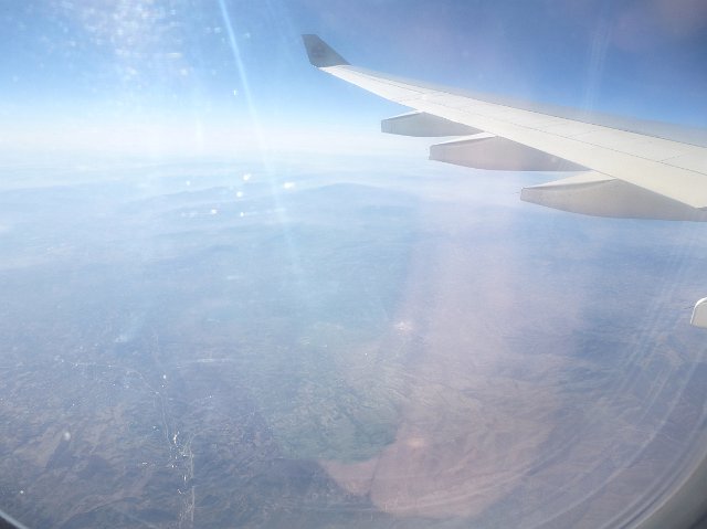 Sun glare or flare on a plane cabin window with a view to the wing outside in a blue sky