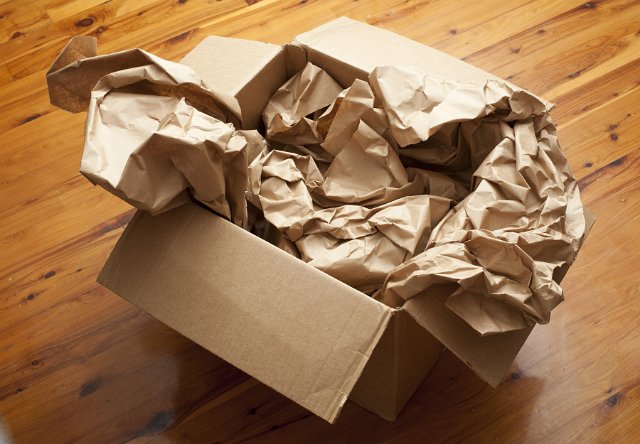Open brown cardboard box with crumpled brown paper inside for packaging and storage viewed high angle on a wooden floor