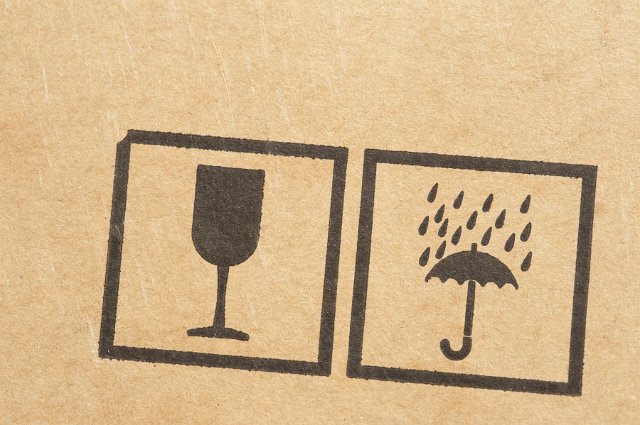 Shipping symbols stamped on a brown cardboard box with a glass for fragility and umbrella warning against getting the contents wet