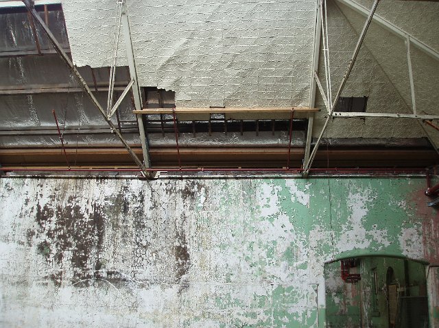 Grunge wall in an industrial warehouse with flaking paint and dark damp stains under roof trusses
