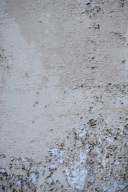 Grey background with old paint decaying and peeling off the concrete or metal surface due to dampness. Close-up full frame view