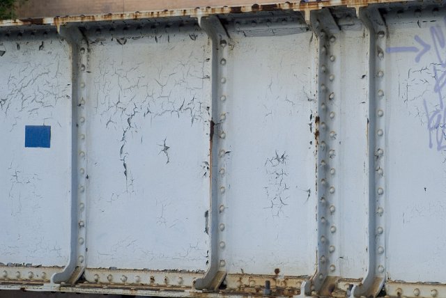 Old rusting structural metal beam with riveted panels and cracked flaking paint