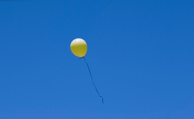 a bright yellow balloon floating in a blue sky
