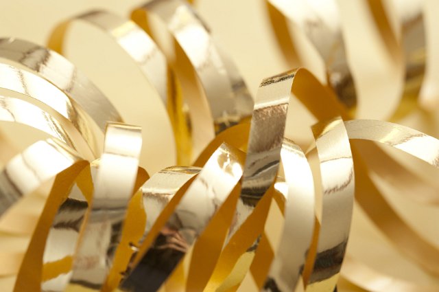 Close up of coiled metallic gold ribbons for a festive celebration on a yellow background, suitable as a Christmas theme