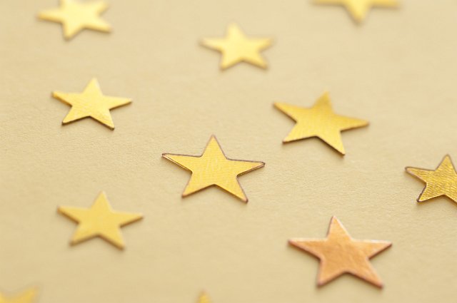 Gold stars, symbolic of the Christmas season or quality, scattered on a yellow background viewed at an oblique angle