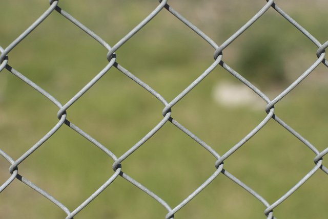 Chain link or diamond mesh fence close up in a full frame symmetrical pattern over blurred green grass