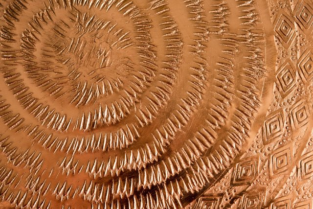 A close up of an embossed, circular pattern on a copper sheet.