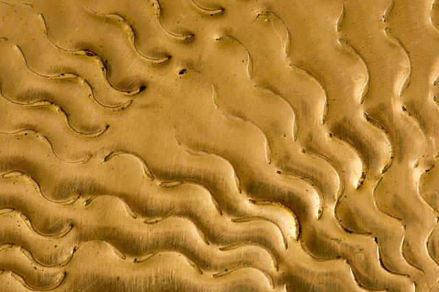 A close up of an embossed, decorative pattern on brass steel.