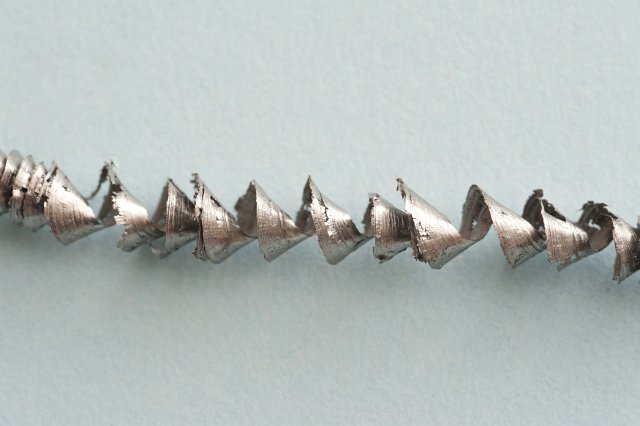 Single twisted spiral metal filing or shaving produced during machining as an industrial waste product on a grey background