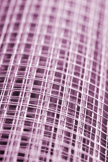 Colorful pink wire grid with square structure in a receding view with selective focus on a roll of steel fencing wire