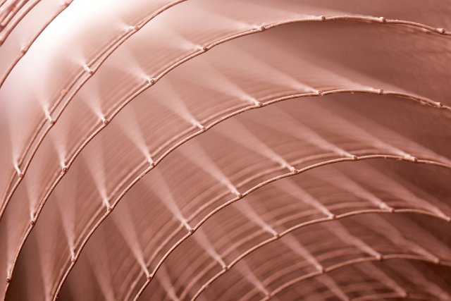 Abstract background pattern of rolled metal mesh looking end on to the edges forming concentric circles in coppery colored light