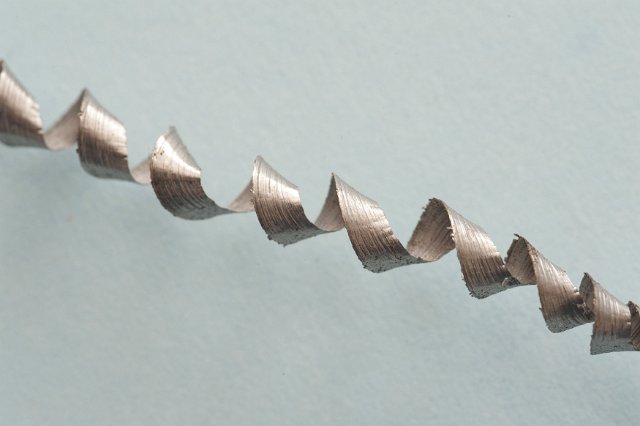 Close up on the structure of a spiral metal shaving viewed diagonally on a grey background with copy space
