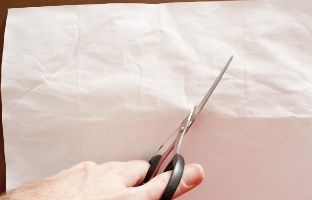 scissors cutting a sheet of rustic looking off white paper