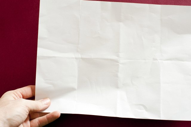a hand holding a sheet of plain white paper with crease marks