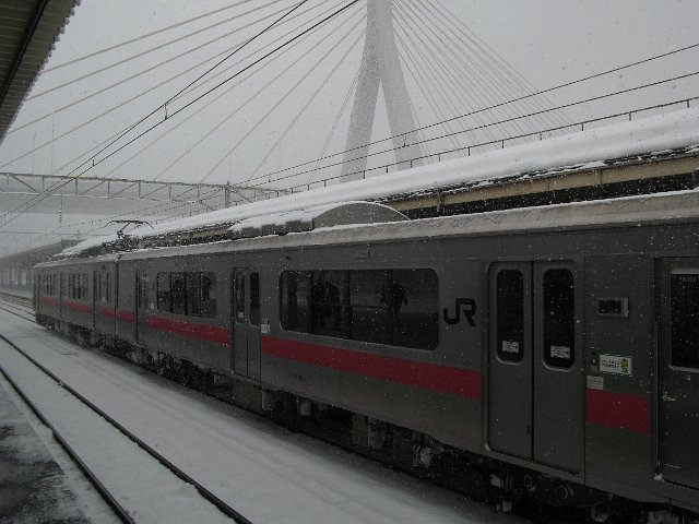 a JR train waiting at a ralway station platform with falling snow