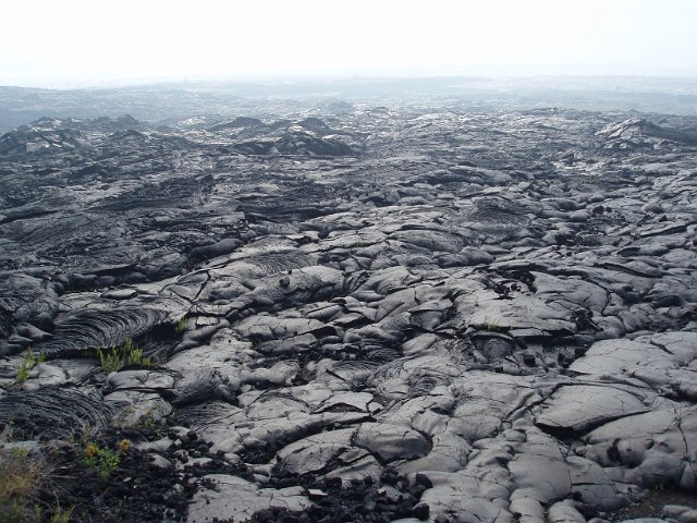 broken surface of a solidified lava field with volcanic gasses in the background