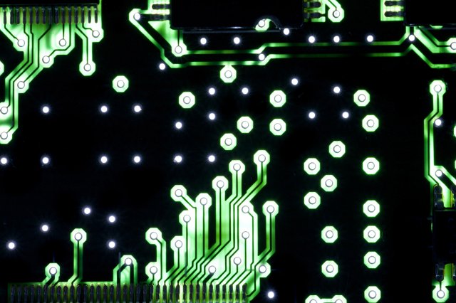 A close up of green, electrical circuit tracks on a black motherboard.