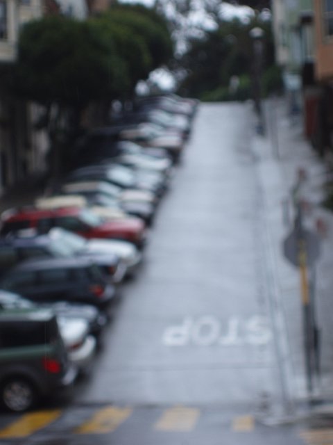 a defocused image of a steep road hill with stop painted on the street
