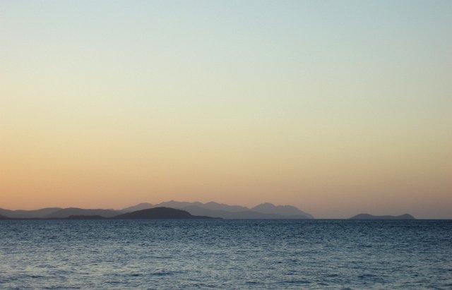 dusky pink sunset with distant land seen over a still ocean