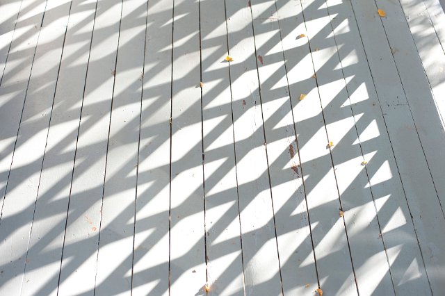Background texture of a painted wooden deck with diamond shadows thrown by a trellis
