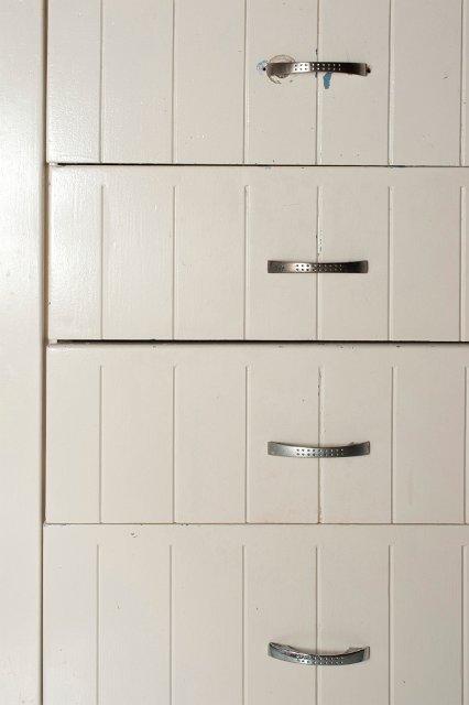 Close up of a set of closed white wooden drawers with a textured surface and metal handles