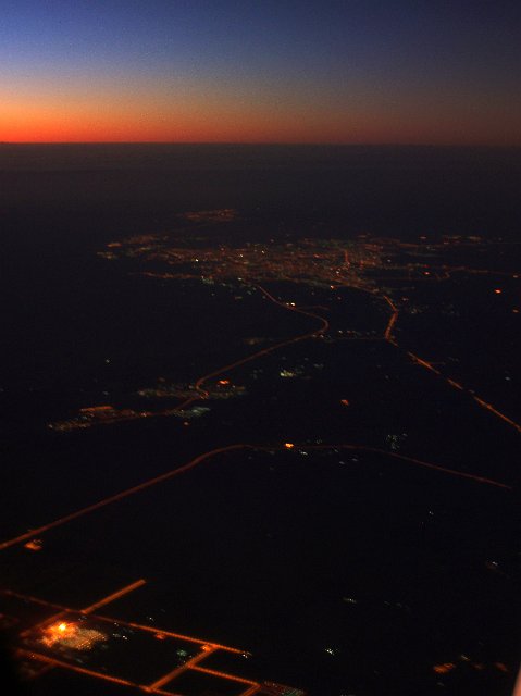 A high aerial landscape of a city, roads and lights after sunset.