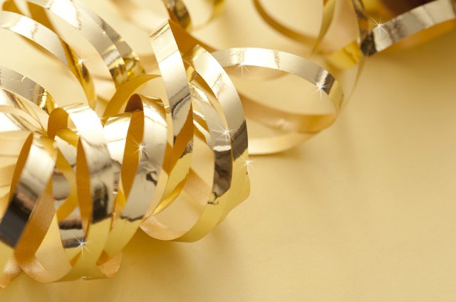 Coiled metallic gold ribbon on a golden background with copyspace for your Christmas, birthday, New Year or festive seasonal greeting
