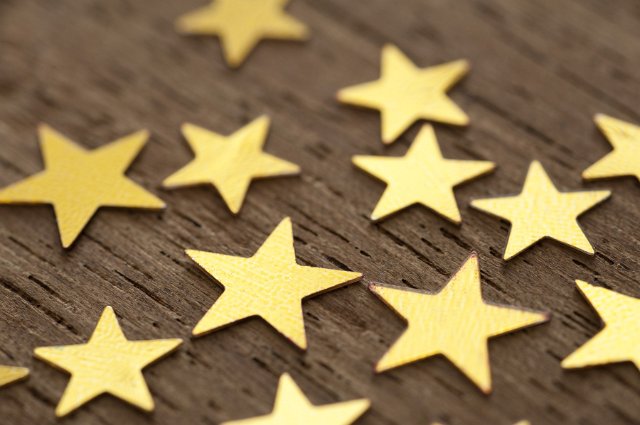 Gold star background pattern with metallic golden stars scattered on textured wood viewed at an oblique angle with shallow dof