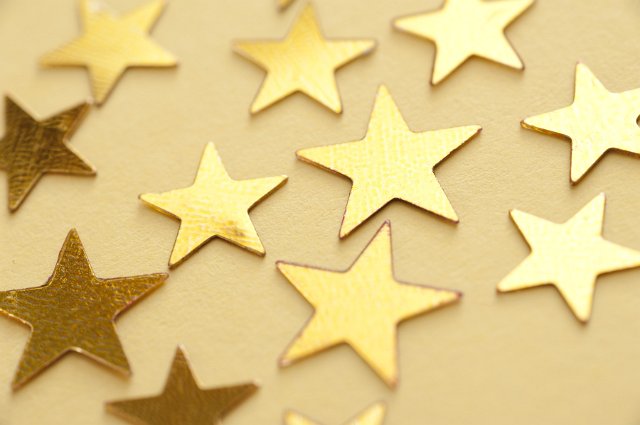Festive gold stars scattered on a golden yellow background viewed at an oblique angle with focus to the central two stars in a festive or Christmas background