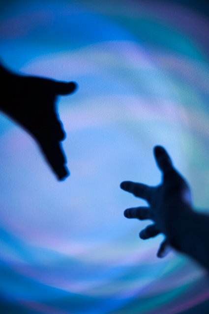 a hand reaching out to meet its own shadow in blue light