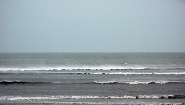 a view out to sea during a cyclone, strong wind blows the tops of breaking waves